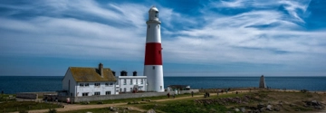 Lighthouse and coastal building beside the sea under a blue sky.