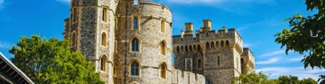 Stone castle towers under a bright blue sky with green trees in the foreground.