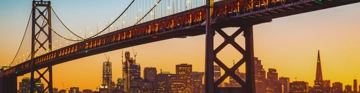 Suspension bridge over a city skyline at sunset.