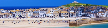 Sandy beach with boats and seaside houses on a hillside by the sea.