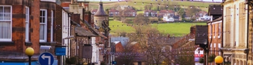 View down a town street towards green fields and houses in the distance.