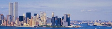 City skyline with twin towers beside the water under a pale blue sky.